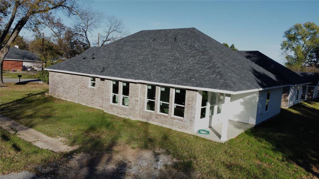 Rear view of house featuring a yard, a patio area, brick siding, and a shingled roof
