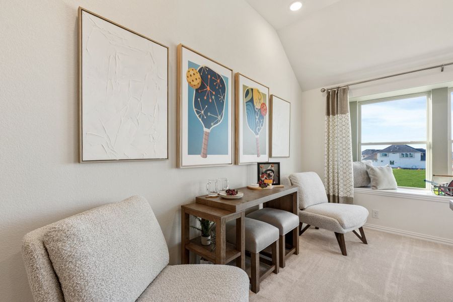 Sitting room with vaulted ceiling, two gray chairs, wood console table, and framed wall art near a large window