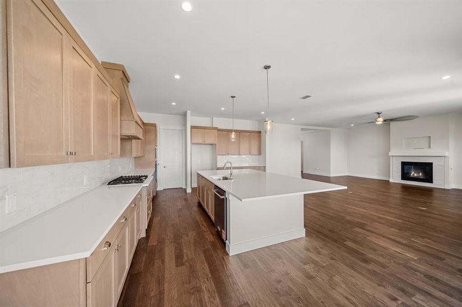 Kitchen featuring hanging light fixtures, a center island with sink, backsplash, a ceiling fan, and dark wood-type flooring