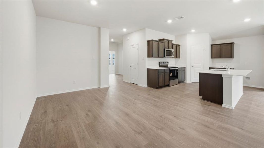 Kitchen with stainless steel appliances, light wood-style floors, dark brown cabinets, a kitchen island with sink, and recessed lighting Kitchen with stainless steel appliances, light wood-style floors, dark brown cabinets, a kitchen island with sink, and recessed lighting