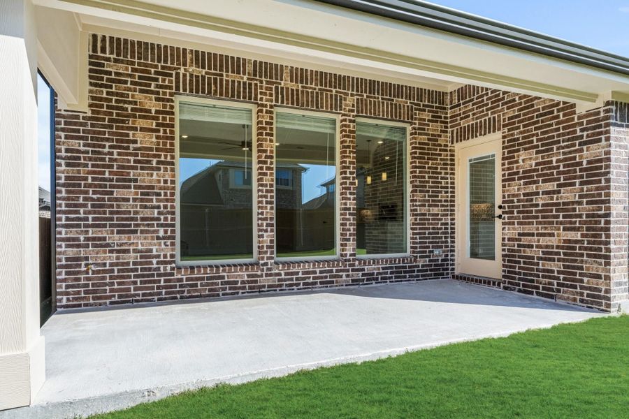 Covered back patio with concrete slab, brick exterior, large windows, and back door entry to home Covered back patio with concrete slab, brick exterior, large windows, and back door entry to home