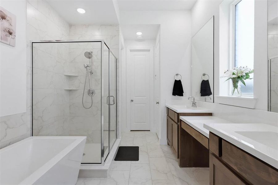 Bathroom featuring a frameless glass shower enclosure, a freestanding soaking tub, dual vanity with wood-finish cabinetry, and tiled flooring