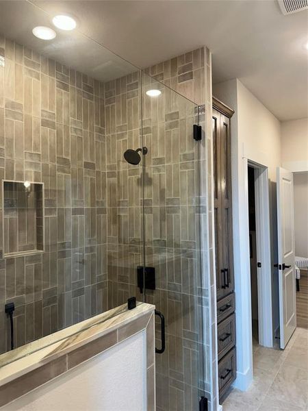 Walk-in shower with clear glass enclosure and matte black fixtures, featuring a recessed niche and vertical tile detailing