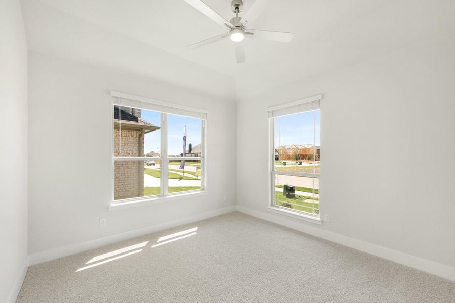 Empty bedroom with carpet, ceiling fan, vaulted ceiling, and two windows overlooking a neighborhood