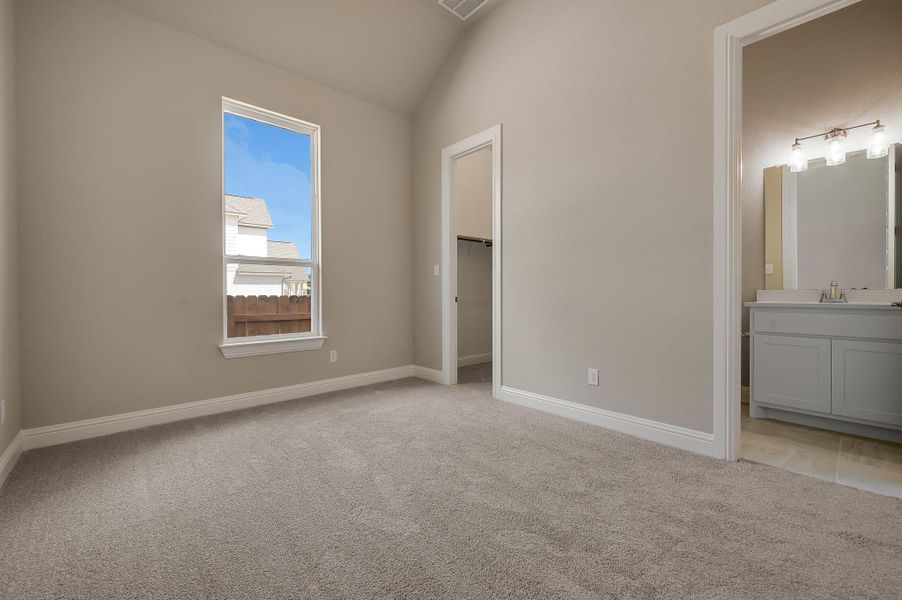 Unfurnished bedroom with light colored carpet, a spacious closet, lofted ceiling, and connected bathroom