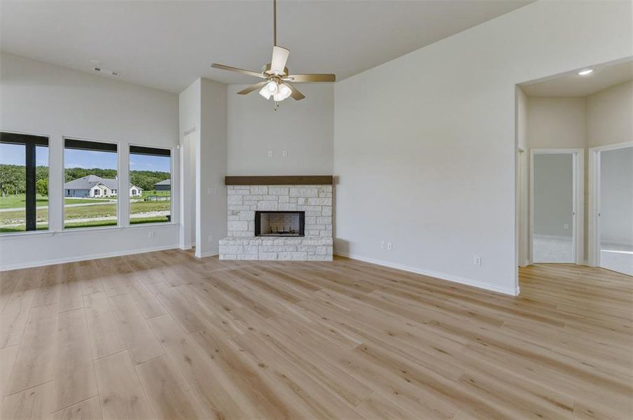 Spacious living area featuring wood-finish flooring, a stone fireplace with a wood mantel, and multiple large windows Spacious living area featuring wood-finish flooring, a stone fireplace with a wood mantel, and multiple large windows