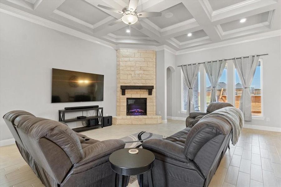 Living area featuring beam ceiling, coffered ceiling, a stone fireplace, and baseboards