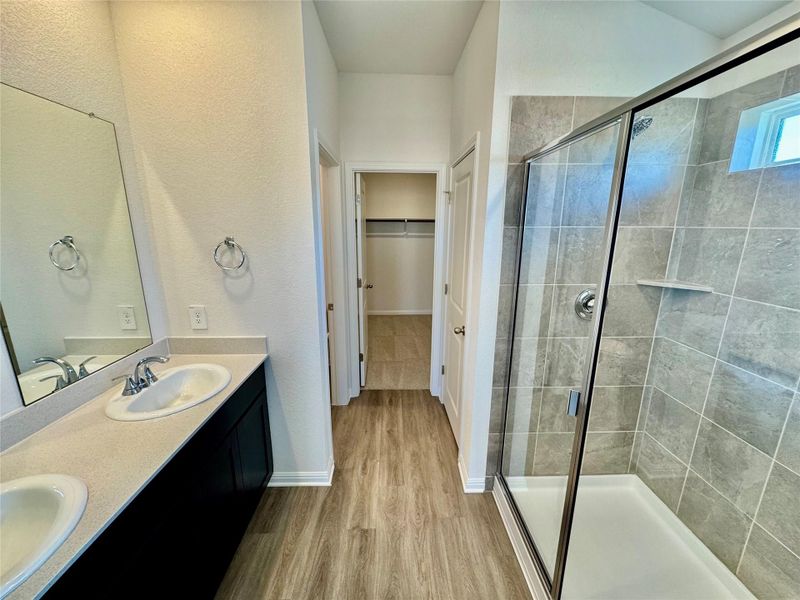 Bathroom featuring double vanity, a walk in closet, light wood-style flooring, a shower stall, and a textured wall Bathroom featuring double vanity, a walk in closet, light wood-style flooring, a shower stall, and a textured wall
