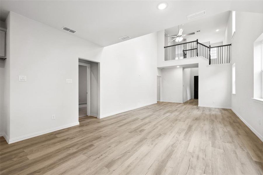 Unfurnished living room with a ceiling fan, light wood finished floors, recessed lighting, baseboards, and a high ceiling Unfurnished living room with a ceiling fan, light wood finished floors, recessed lighting, baseboards, and a high ceiling