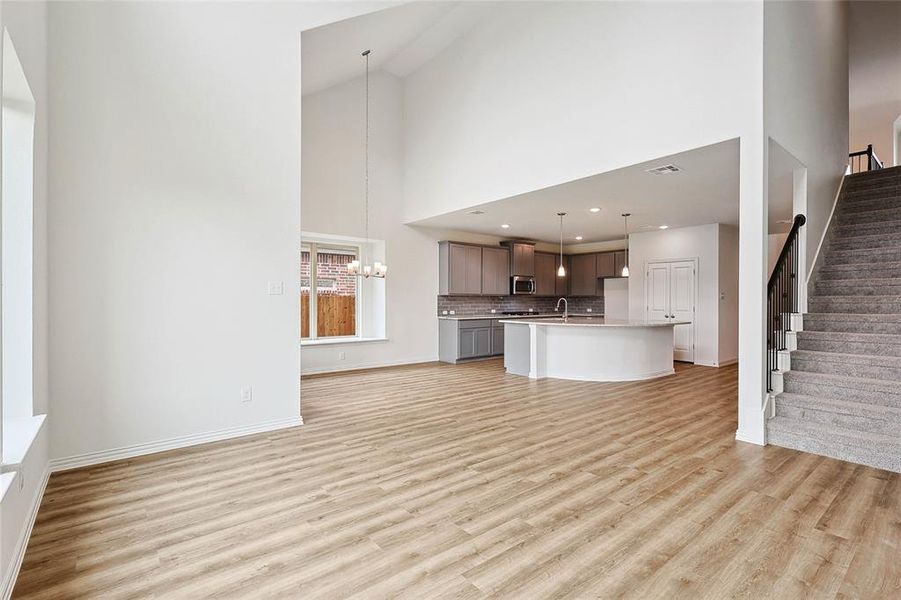 Unfurnished living room with high vaulted ceiling, sink, an inviting chandelier, and light wood-type flooring