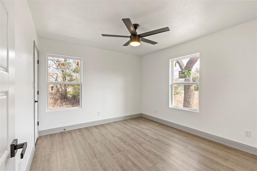 Unfurnished room with light wood finished floors, a ceiling fan, plenty of natural light, and a textured ceiling