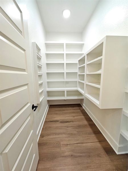 This photo showcases a spacious walk-in pantry with ample white shelving for storage, wood flooring, and bright lighting, ideal for organizing kitchen essentials.