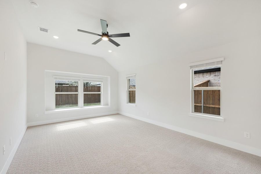 Empty bedroom with vaulted ceiling, ceiling fan, carpet flooring, and multiple windows