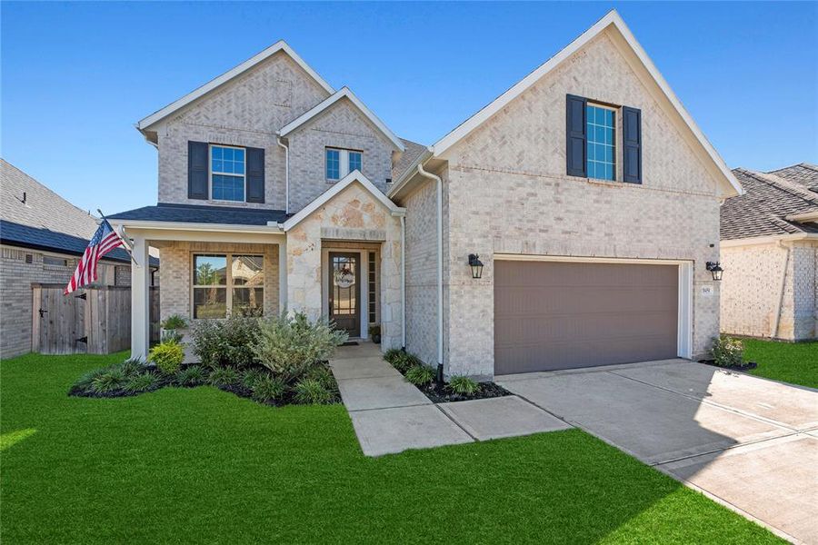 This is a two-story home featuring a brick facade, a two-car garage, and a well-manicured lawn. It includes a front porch and a welcoming atmosphere.