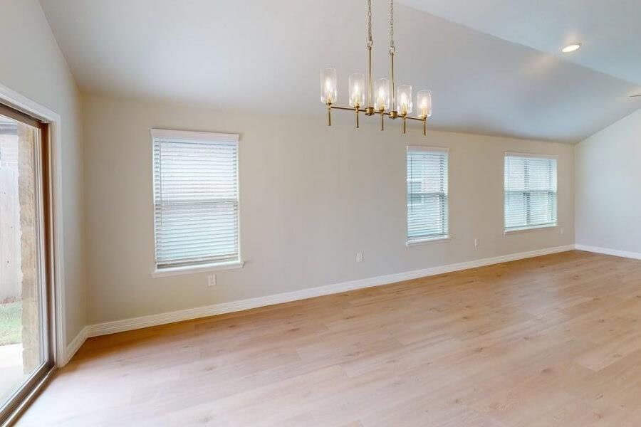 Spare room with lofted ceiling, plenty of natural light, light wood-style flooring, and a chandelier