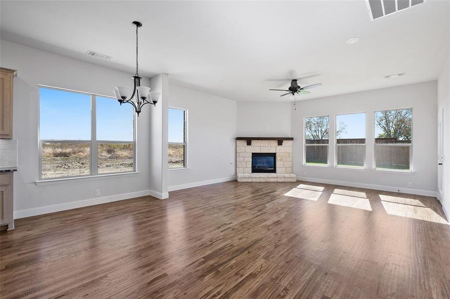 Unfurnished living room with a ceiling fan, a fireplace, dark wood finished floors, and a chandelier