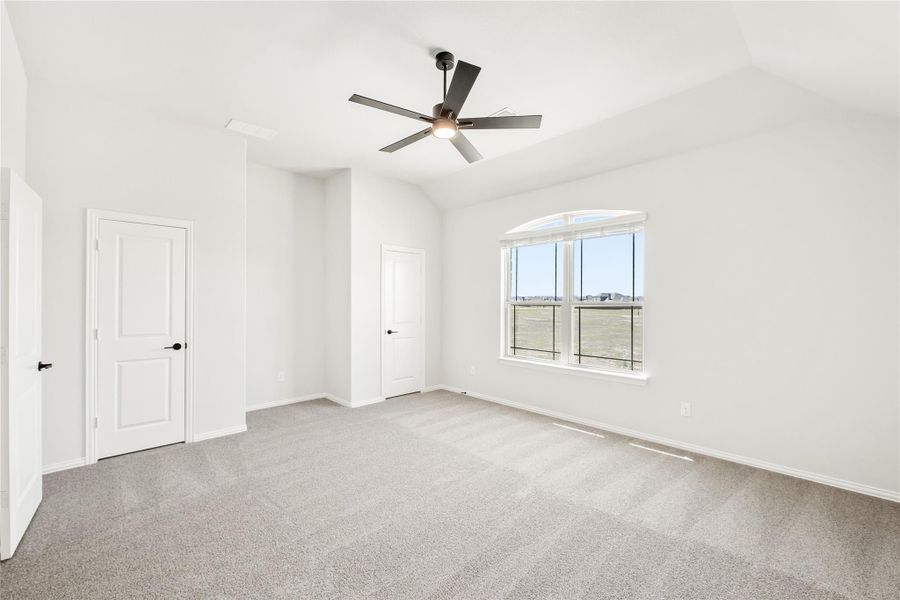 Empty bedroom with vaulted ceiling, ceiling fan, gray carpet, and arched window