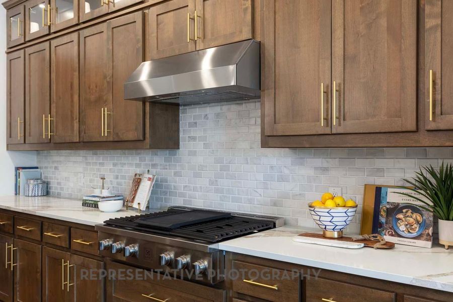 Kitchen with wall chimney exhaust hood, stainless steel gas cooktop, tasteful backsplash, and glass insert cabinets Kitchen with wall chimney exhaust hood, stainless steel gas cooktop, tasteful backsplash, and glass insert cabinets