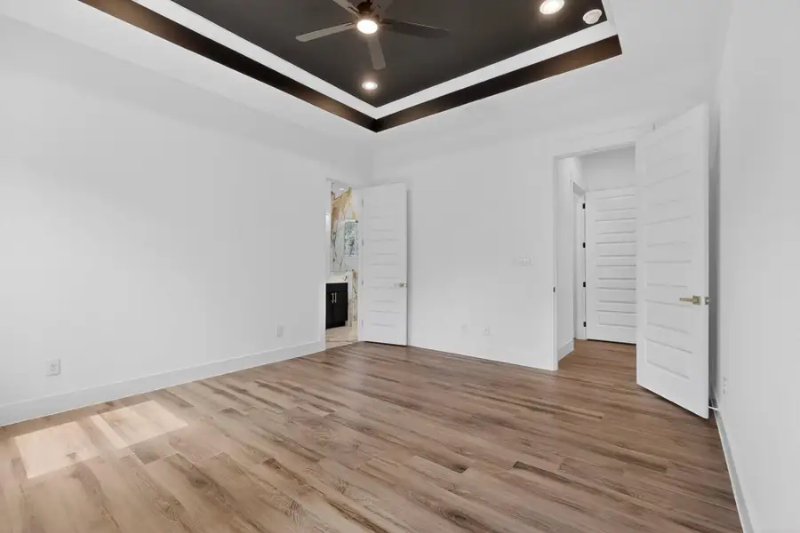 Recessed lighting and a ceiling fan adorn the tray ceiling in this spacious bedroom with wood flooring.