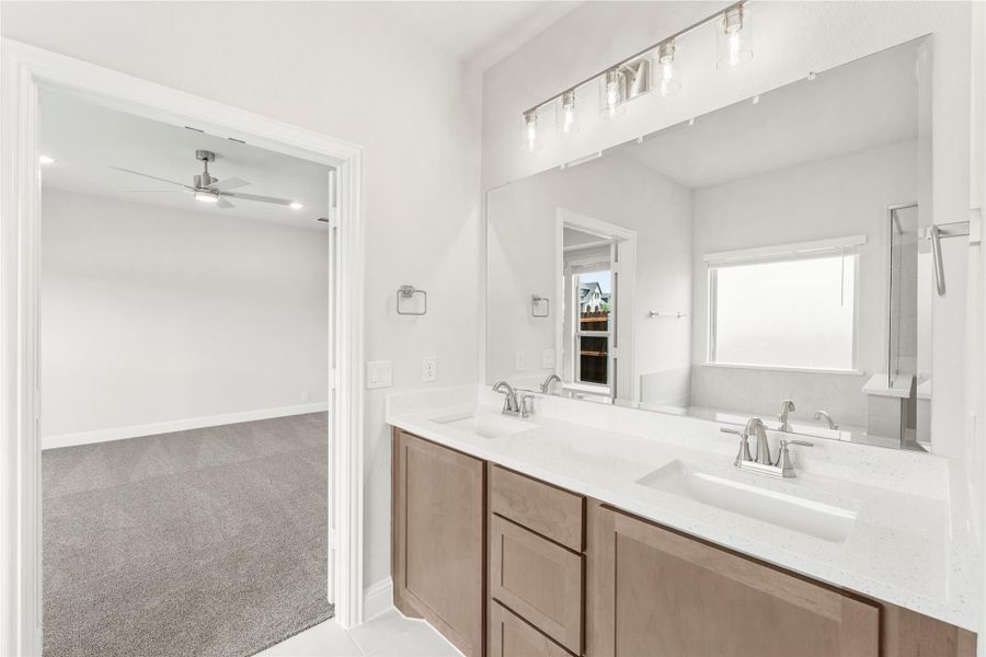 Bathroom with double sink vanity, wood cabinets, white countertops, and large mirror with overhead lighting