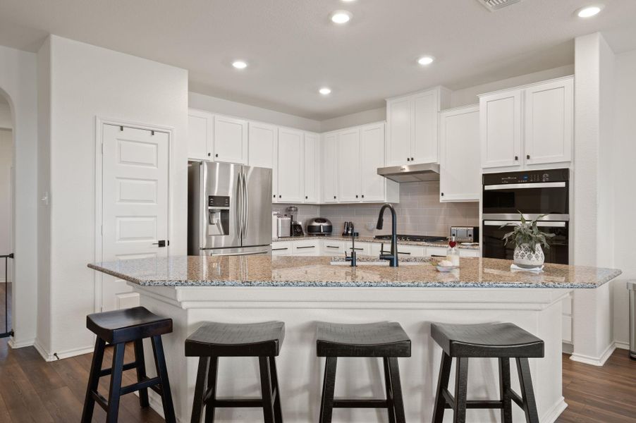 Kitchen with white cabinetry, dark wood-style flooring, light stone countertops, stainless steel appliances, and a breakfast bar area