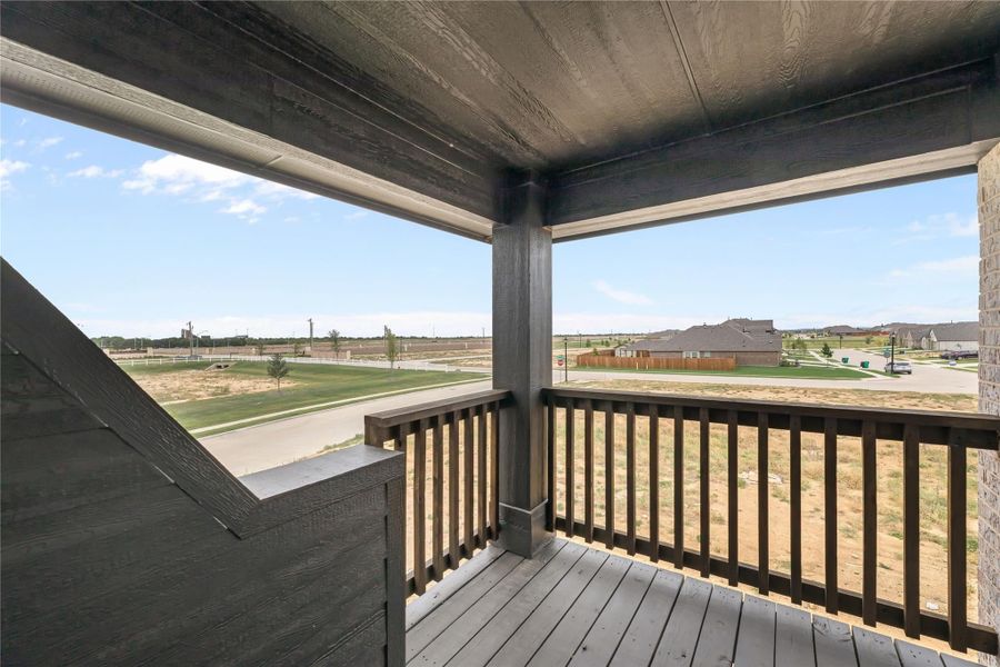 Covered second-floor balcony with dark wood railing overlooking a suburban neighborhood and open fields Covered second-floor balcony with dark wood railing overlooking a suburban neighborhood and open fields