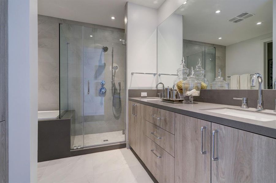 Primary bathroom outfitted with dual vanities, frameless glass shower with bench seat and soaking tub.  Large walk-in closet and dual storage cabinets complete the space.