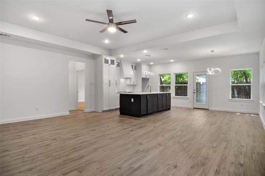 Unfurnished living room with plenty of natural light, light wood-type flooring, and ceiling fan with notable chandelier