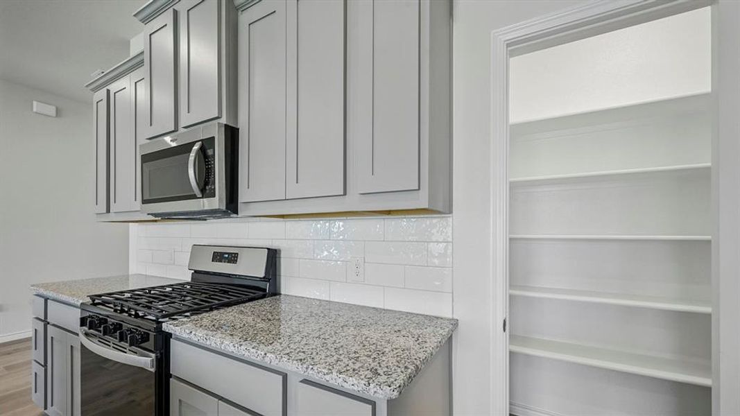 Kitchen with stainless steel appliances, gray cabinets, light stone counters, and backsplash