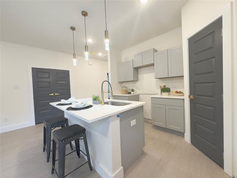 Kitchen featuring a kitchen island with sink, pendant lighting, light hardwood / wood-style flooring, backsplash, and sink