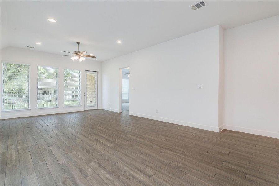 This expansive room features plank-style flooring, white walls, and a ceiling fan with integrated lighting