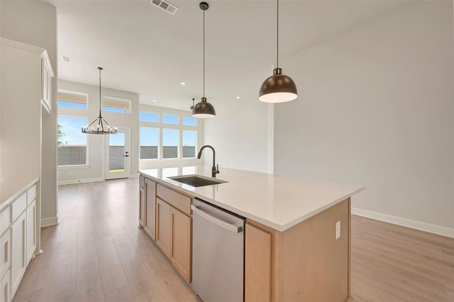 Kitchen island featuring a stainless steel sink, gooseneck faucet, light wood-finish cabinetry, and a light-toned countertop