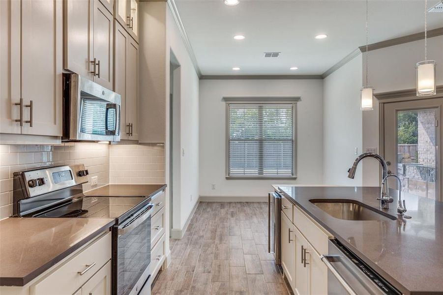 Kitchen with stainless steel appliances, dark stone counters, ornamental molding, wood finish floors, and hanging light fixtures Kitchen with stainless steel appliances, dark stone counters, ornamental molding, wood finish floors, and hanging light fixtures