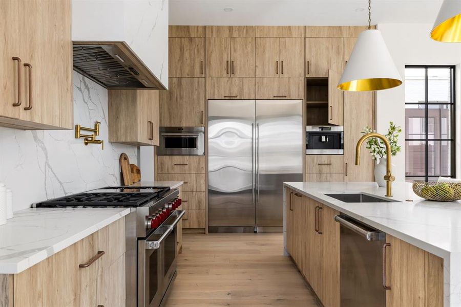 Kitchen with light stone countertops, premium appliances, light wood-style floors, hanging light fixtures, and backsplash Kitchen with light stone countertops, premium appliances, light wood-style floors, hanging light fixtures, and backsplash