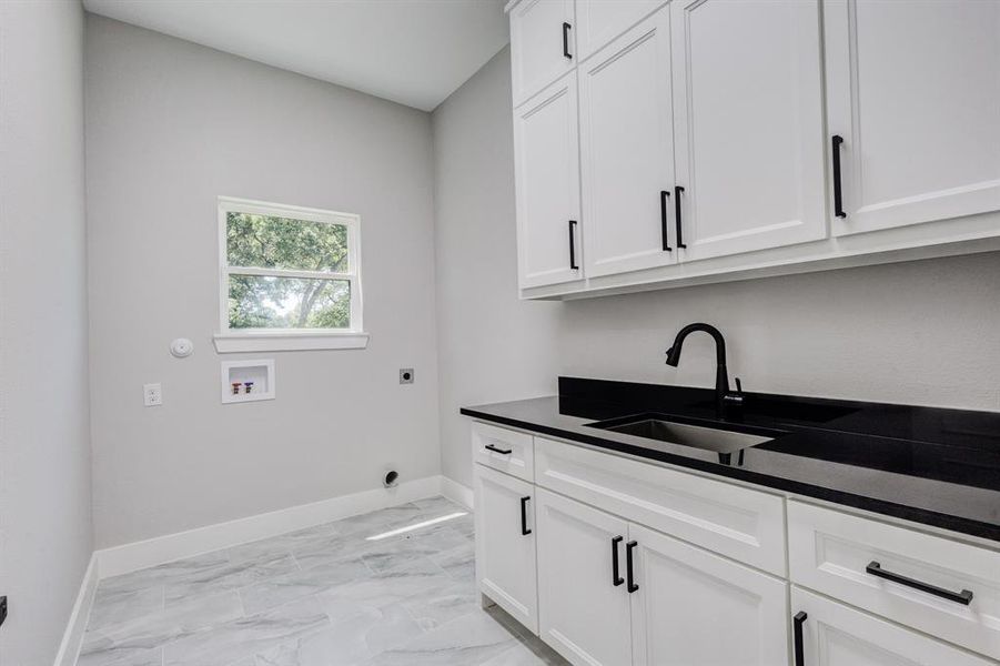 Laundry room featuring white cabinetry with black hardware, a black countertop, and an undermount sink with a matte black faucet