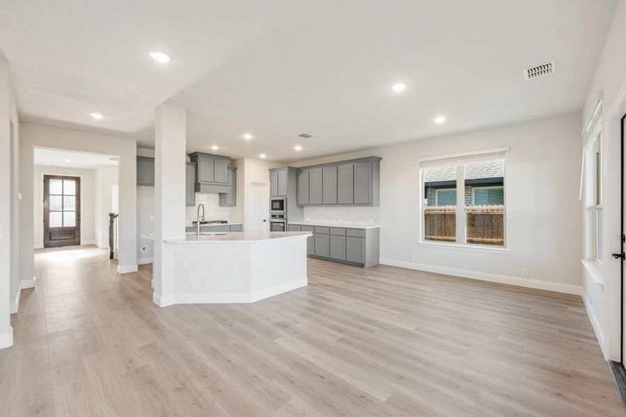 Open-concept kitchen and living area with gray cabinets, white island, and light hardwood floors Open-concept kitchen and living area with gray cabinets, white island, and light hardwood floors