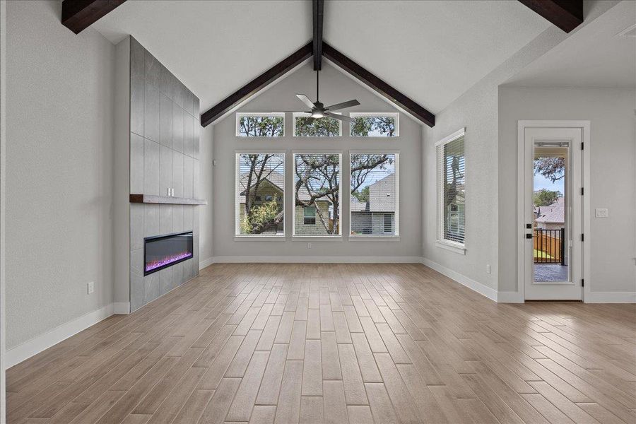 Unfurnished living room with beamed ceiling, a fireplace, light wood-style flooring, plenty of natural light, and a ceiling fan Unfurnished living room with beamed ceiling, a fireplace, light wood-style flooring, plenty of natural light, and a ceiling fan