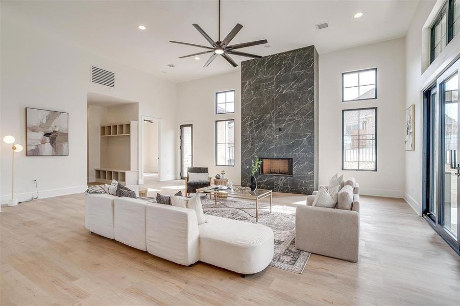 Living area featuring a high ceiling, a high end fireplace, recessed lighting, light wood-type flooring, and a ceiling fan