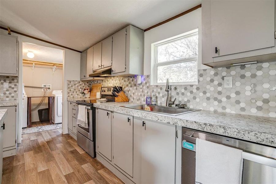 Kitchen featuring tasteful backsplash, washer / dryer, sink, light hardwood / wood-style flooring, and appliances with stainless steel finishes