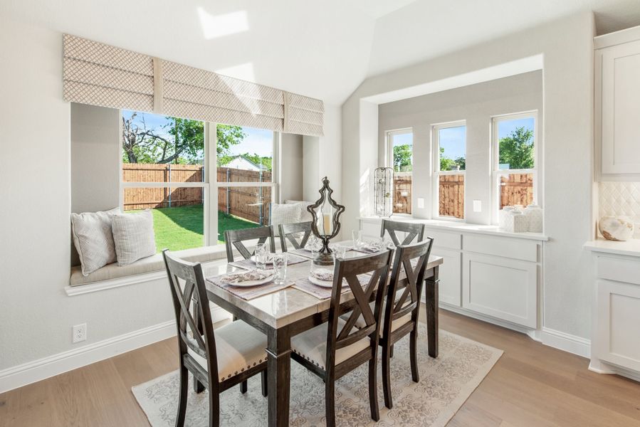 Bright dining area with dark wood table, four chairs, window seat, and large windows overlooking backyard