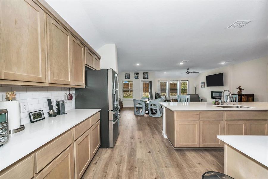 Kitchen featuring light wood-type flooring, tasteful backsplash, stainless steel fridge with ice dispenser, ceiling fan, and sink