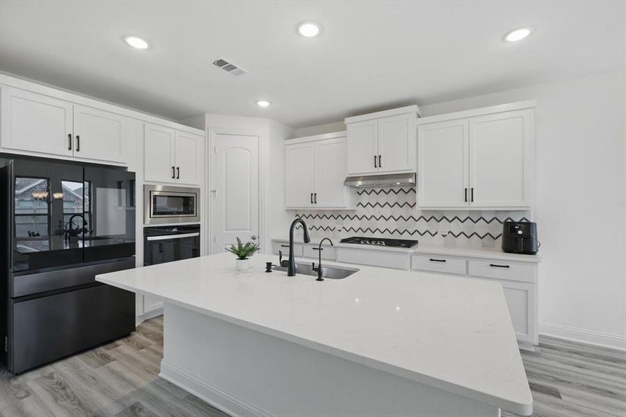 Kitchen featuring black appliances, white cabinetry, light stone counters, recessed lighting, and light wood finished floors