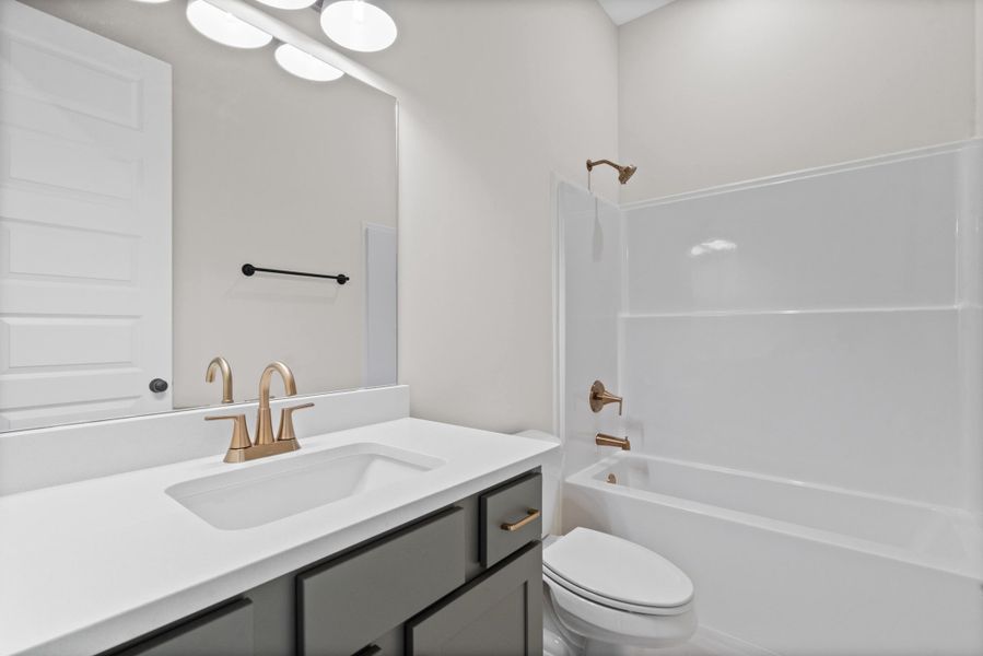 Bathroom featuring a single vanity with a white countertop, gold-finish faucet, and gray cabinetry Bathroom featuring a single vanity with a white countertop, gold-finish faucet, and gray cabinetry