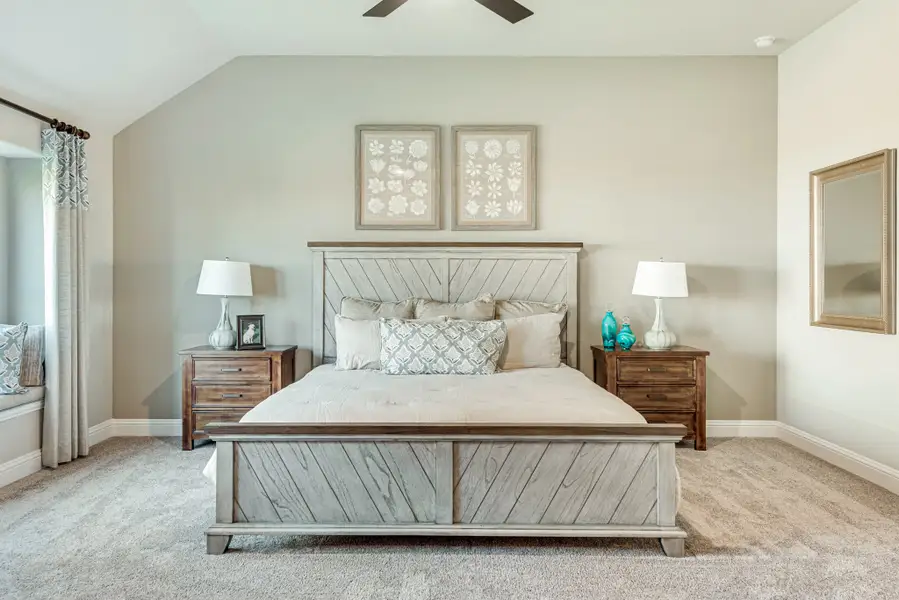 Bedroom with wood panel bed frame, vaulted ceiling, ceiling fan, and two nightstands on carpet flooring