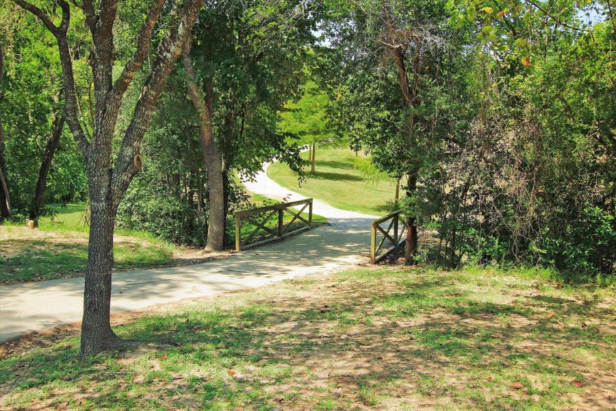 Terry Hershey Park's charming wooded pathway featuring a quaint bridge crossing and shaded canopy of mature trees. Natural surroundings create a tranquil retreat ideal for leisurely walks and outdoor enjoyment. The gently curving trail and layered greenery provide a scenic extension of the neighborhood’s active, nature-connected setting.