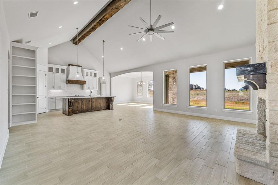 Unfurnished living room featuring beam ceiling, high vaulted ceiling, light wood-style floors, arched walkways, and recessed lighting