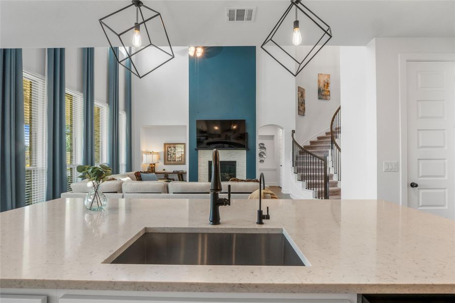 Kitchen with a kitchen island with sink, light stone countertops, a high ceiling, a glass covered fireplace, and pendant lighting Kitchen with a kitchen island with sink, light stone countertops, a high ceiling, a glass covered fireplace, and pendant lighting