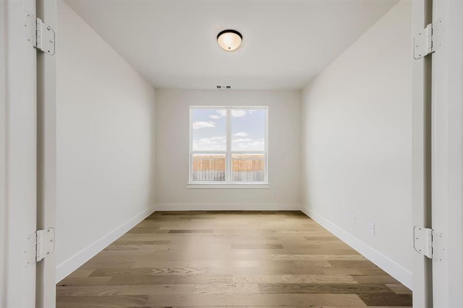 Well-lit room featuring wood-finish flooring, white baseboards, and a single window with a white frame