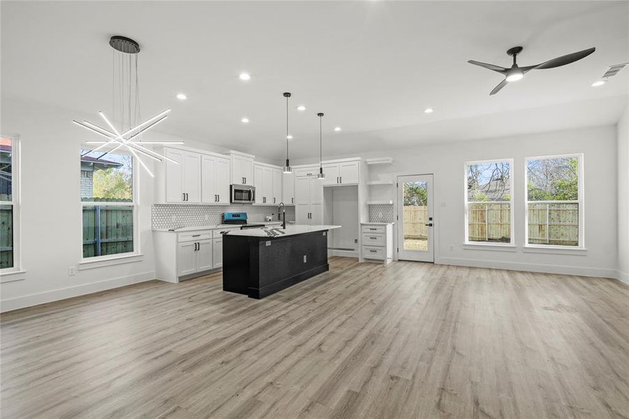 Kitchen with white cabinetry, hanging light fixtures, light hardwood / wood-style flooring, backsplash, and a center island with sink