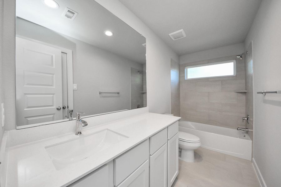 Secondary bath features tile flooring, bath/shower combo with tile surround, light stained wood cabinets, beautiful light countertop. Sample photo of completed home with similar floor plan. Actual colors and selections may vary.